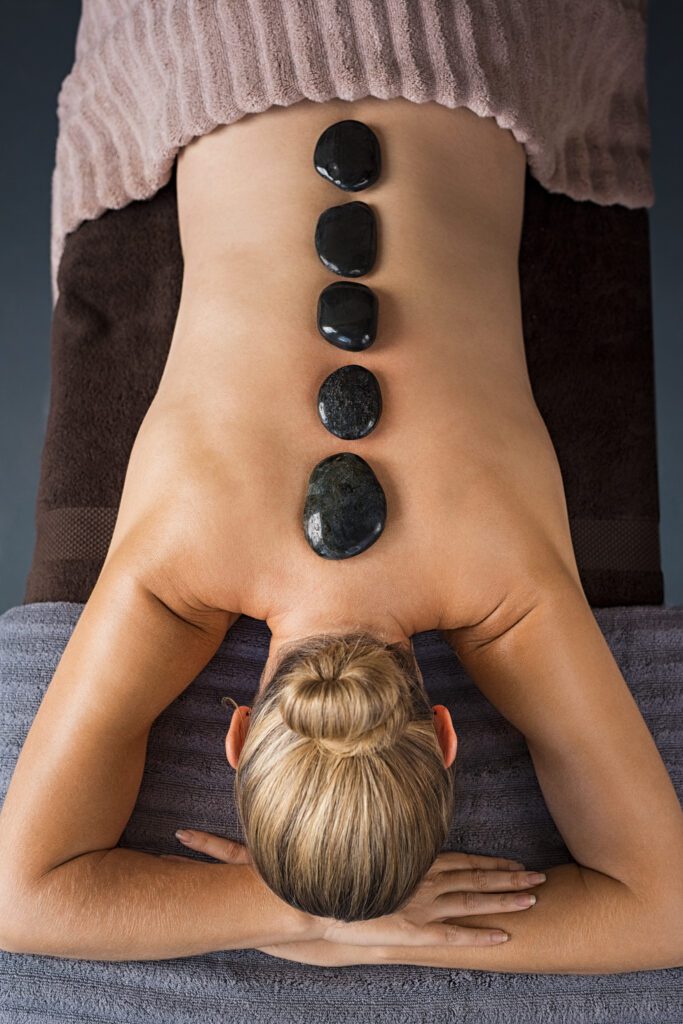 Top view of mature woman relaxing during hot stone massage. High angle view of senior woman back in a wellness spa receiving lastone therapy. Senior woman enjoying a hot stone treatment.